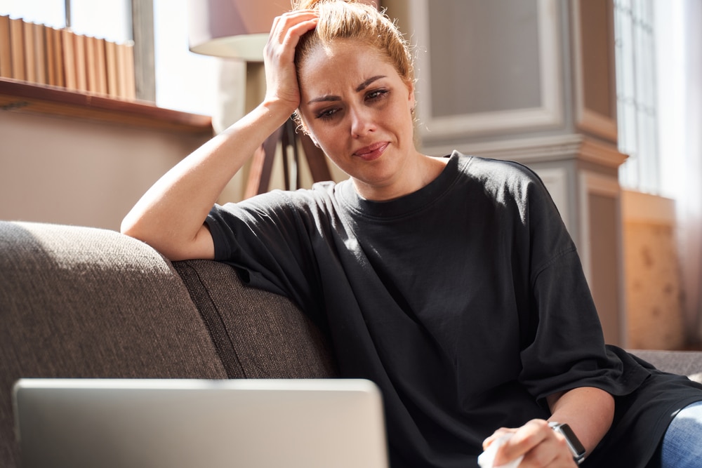 Woman sitting on sofa with hand propping up head. Tears are disrupting her heavy make-up.